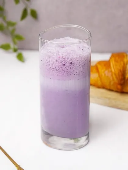 A layered blueberry smoothie in a glass, an effective shot for a specialty beverage menu.