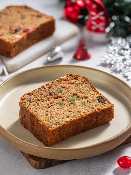 A slice of classic fruit cake, showing the colorful candied fruits inside, styled for a Christmas menu.