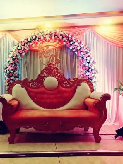 This elegant decor for an engagement features a floral ring backdrop, beautiful drapery, and a regal red and white sofa, creating a perfect stage for the happy couple.