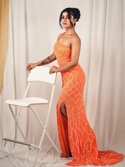 A full-body shot showcasing the elegant silhouette of the one-shoulder orange sequin gown. The fit is designed to flatter your curves beautifully.