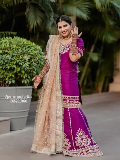 A stunning bride in a purple sharara, showing off her full-arm mehndi. The design complements her royal outfit perfectly.