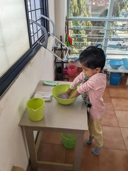 This child is engaged in a washing activity. Practical life skills like this help children develop independence, coordination, and a sense of responsibility for their environment.