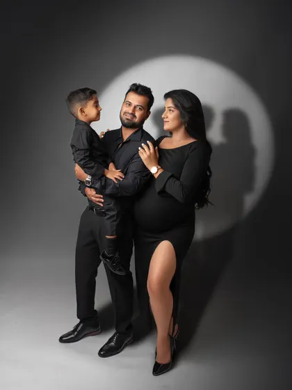 Celebrating the journey to parenthood with a classic, dramatic studio portrait. This maternity session uses a spotlight effect and coordinated black outfits to create a sophisticated and timeless family photograph.