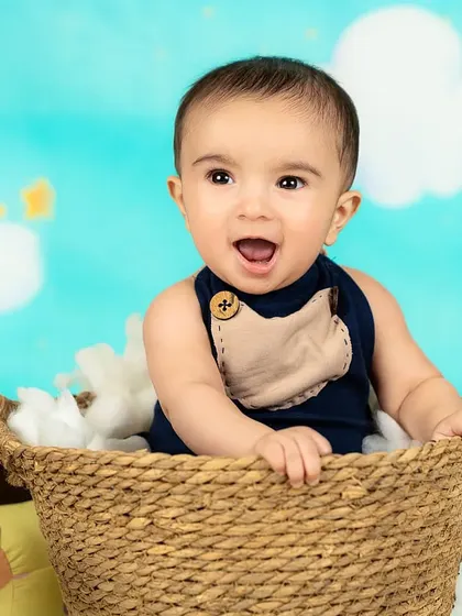 A joyful baby boy laughs with excitement from his basket in the clouds.