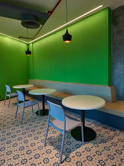 A simple yet inviting cafe nook with a bright green accent wall, built-in banquette seating, and patterned floor tiles.