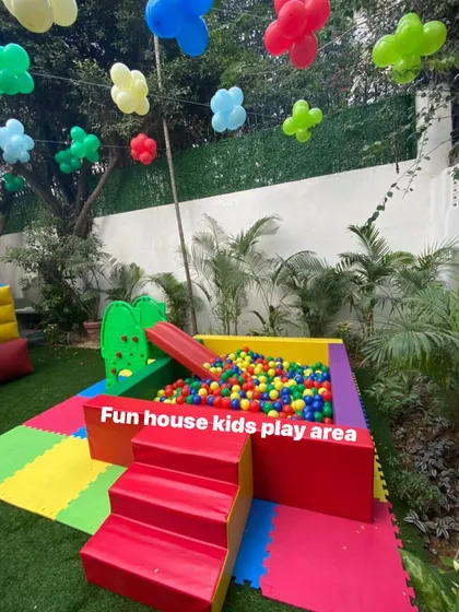 The rainbow ball pit and slide set up in a backyard, surrounded by festive balloons.