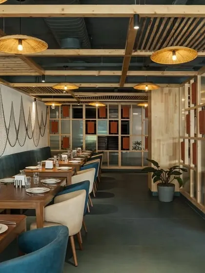 The design incorporates coastal elements, like the draped fishing nets on the wall, in a contemporary way. The blue and beige chairs and wooden furniture complete the relaxed, seaside-inspired theme.