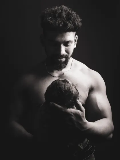 A dramatic black and white photo of a father holding his newborn. The lighting is carefully controlled to create a powerful and emotional image that emphasizes the father's protective embrace.