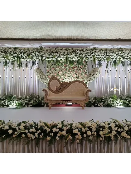 For engagements and receptions, I create sophisticated floral backdrops. This elegant white-on-white stage design uses a dense wall of flowers and a classic chaise lounge to create a timeless and romantic setting for the couple.