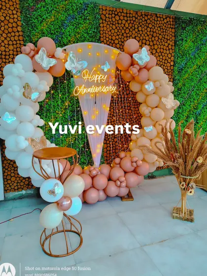 A whimsical anniversary backdrop featuring a circular balloon arch in pastel pinks and whites. I added butterfly cutouts and a 'Happy Anniversary' neon sign to create a soft, romantic theme for the celebration.
