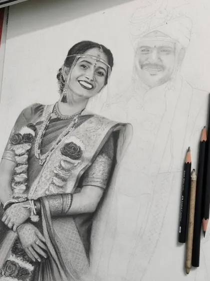 This image shows a wedding portrait in progress. The bride is almost fully rendered with detailed shading on her saree and jewelry, while the groom is still a light pencil outline, showing the contrast between the start and the finish.