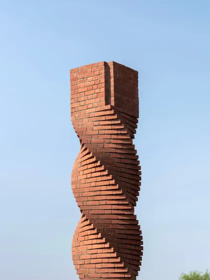 **The Urban Twist, Ahmedabad:** A close-up of the column against a clear blue sky emphasizes its sculptural form. The precise, layered brickwork creates a sense of movement and modern craftsmanship.