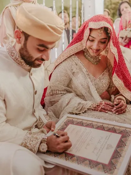 The groom signs the Nikah register as his bride looks on, a significant and solemn moment in their wedding ceremony.