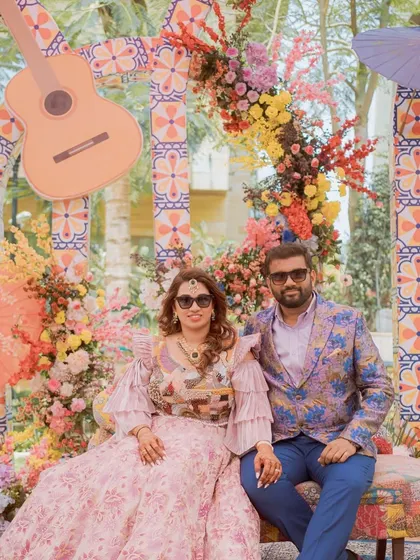 The couple poses at their Mexican-themed Mehendi. The colorful floral arch with a guitar prop creates a perfect, thematic backdrop for their portraits.