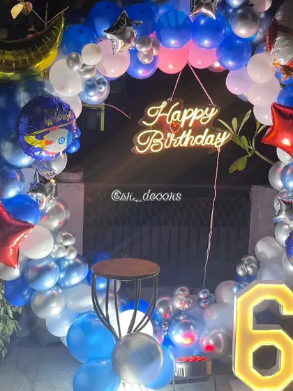 A vibrant outdoor 'Space' theme for a 6th birthday, using a circular balloon frame with astronaut and moon foil balloons, a neon sign, and a light-up number.