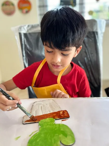 The first step is painting the base. This young artist is carefully applying a coat of brown paint to the pot of his cactus cutout.