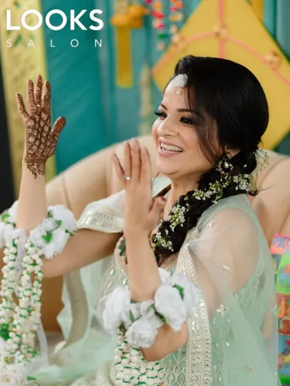 For pre-wedding functions like a Haldi or Mehendi, I aim for a look that is fresh, radiant, and joyful. Here, I used soft, natural makeup to enhance her features, paired with a beautiful floral hairstyle, ensuring she looked effortlessly beautiful while celebrating.