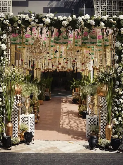 A grand entrance for a Pichwai-themed wedding, featuring lush greenery, floral arches, and a ceiling canopy of hanging flowers and chandeliers. This is the epitome of traditional luxury.