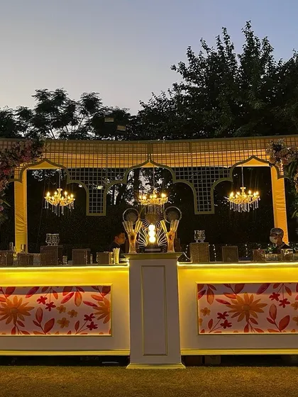 An elegant bar setup for a wedding reception. The custom floral-print bar front, topped with classic chandeliers, adds a touch of bespoke charm to the celebration.