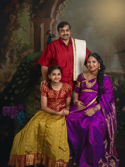 A formal family portrait of an expecting mother with her husband and daughter in a traditional studio setting. Everyone is looking at the camera, creating a timeless keepsake for the family.