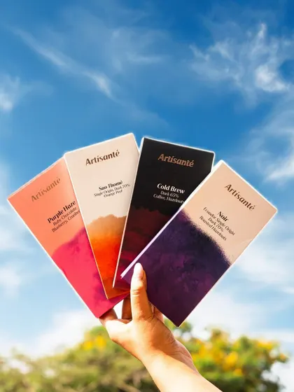 A vibrant lifestyle shot showcasing a range of artisanal chocolate bars against a bright blue sky. This type of user-generated content (UGC) style photography makes the product feel accessible and desirable.