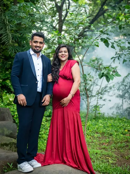 A classic, posed portrait of the expecting couple in a beautiful park. Her red gown and his smart suit create a formal yet warm look, perfect for a timeless maternity photograph.