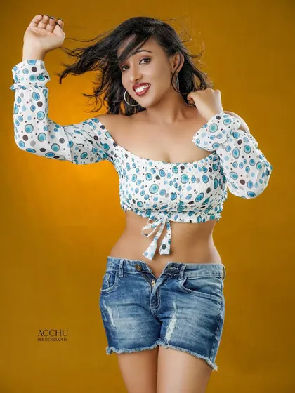 Fun and energetic. This studio portrait captures a playful moment, with a crop top and unbuttoned denim shorts against a bright yellow background for a summery feel.