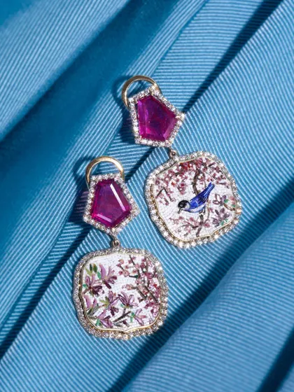 A studio shot of the Sakura micromosaic earrings against a blue backdrop. This pair celebrates the ruby, the birthstone of July, with vibrant, ethically mined gems from Gemfields.