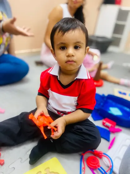 A toddler sits with various toys, including a toy animal and a doctor's kit, engaging in the kind of imaginative free play that is crucial for social and emotional development.