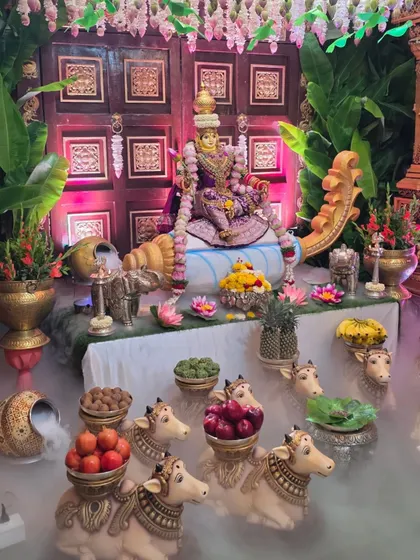 A close-up of my signature Lakshmi doll centerpiece, designed to bring blessings and prosperity. This setup features the goddess seated against a traditional carved wooden door, surrounded by offerings on cow props and an ethereal dry ice fog effect.