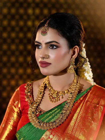 A complete look at a traditional South Indian bride in a stunning green and red Kanjivaram silk saree. The makeup features defined eyes, a bold matte lip, and a flawless base that complements the antique gold jewelry.