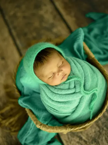 This overhead angle highlights the expert wrapping technique and the baby's perfect form, nestled in a green bonnet and swaddle.