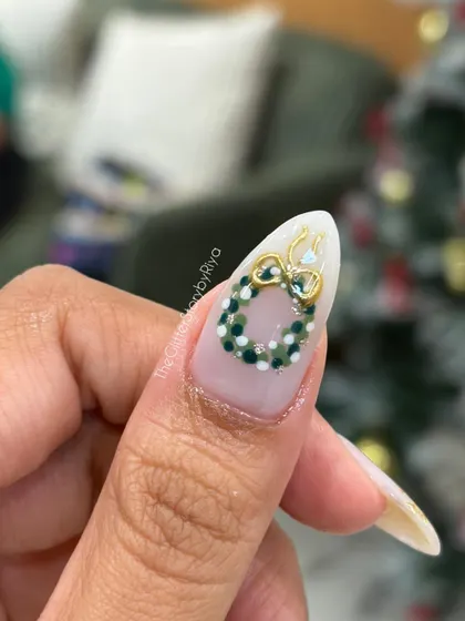 A macro shot of a single nail with a detailed, hand-painted Christmas wreath. The tiny dots and the 3D gold bow show the level of precision involved.