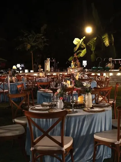 The outdoor seating arrangement for Ezekiel's communion party. The tables are dressed in beautiful blue velvet cloths, complemented by wooden cross-back chairs, creating a rich and elegant dining setting.