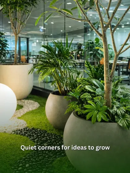 I create quiet corners designed for ideas to grow. This indoor zen garden setup uses a combination of large potted trees, smaller palms, and soft artificial grass with river stones to build a peaceful retreat within the office.