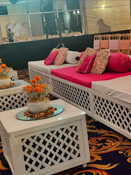 Comfortable and traditional low seating for the Bhaat ceremony. The bright pink cushions and bolsters are paired with intricate white tables, combining comfort with cultural aesthetics.