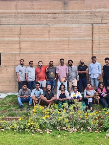 The full team in front of a large rammed earth wall, a signature element of our architectural practice.