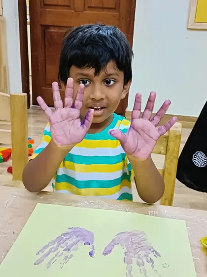 A young boy shows his purple painted hands, ready for an art project. We love capturing these simple, joyful moments.
