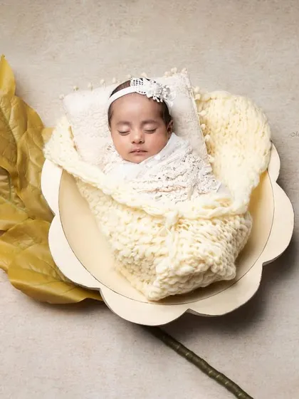 A final portrait from a newborn session, showcasing a creative floral prop setup. The baby is nestled safely in a flower-shaped bowl, wrapped in a soft, textured knit. This is the kind of artistic and memorable image I teach my students to create.
