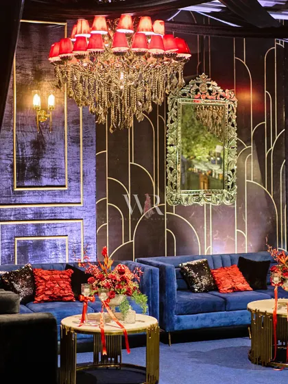 A close-up of a lounge area from the European-themed night. A plush blue velvet sofa is accented with red and sequined cushions, set against a custom Art Deco wall panel.