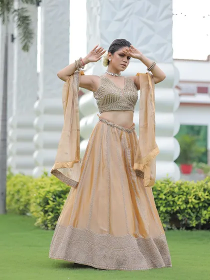 A dramatic pose in the gold lehenga, with the model's arms raised to show the flow of the dupatta.
