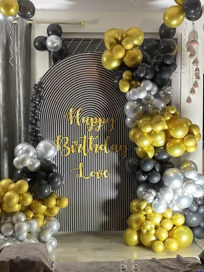 A chic birthday backdrop with a black, gold, and silver balloon arrangement against a striped panel.