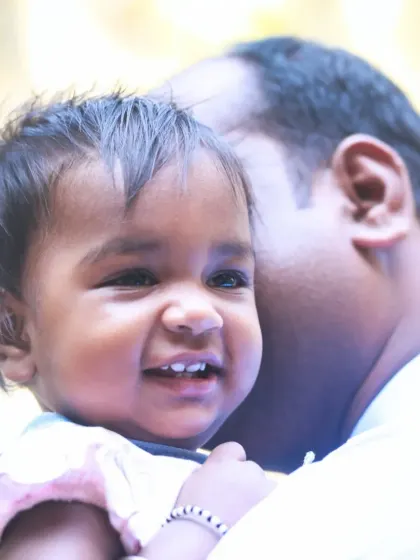 A candid shot of a baby girl's bright, happy smile while being held by her father.