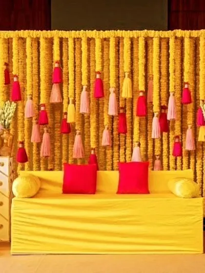 A simple yet elegant Haldi seating setup. The backdrop is made entirely of marigold strings, accented with colorful tassels, creating a classic and vibrant look that is perfect for photos.