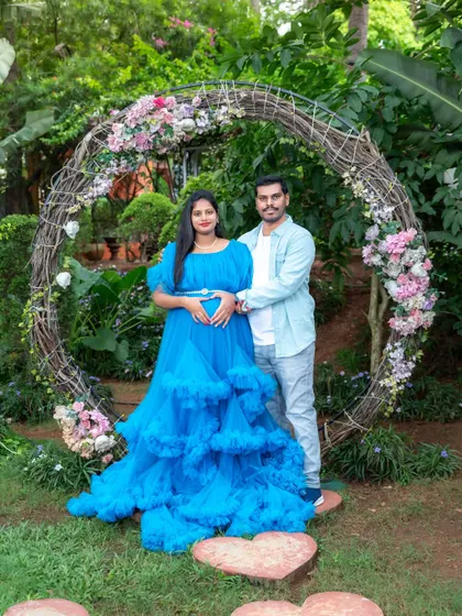 A beautiful couple's portrait in a garden, making a heart shape with their hands over the baby bump. A perfect symbol of their growing love.