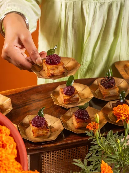A guest holding a delicate appetizer of layered potato and beetroot. The festive orange background and floral elements emphasize the celebratory context of our catering services.