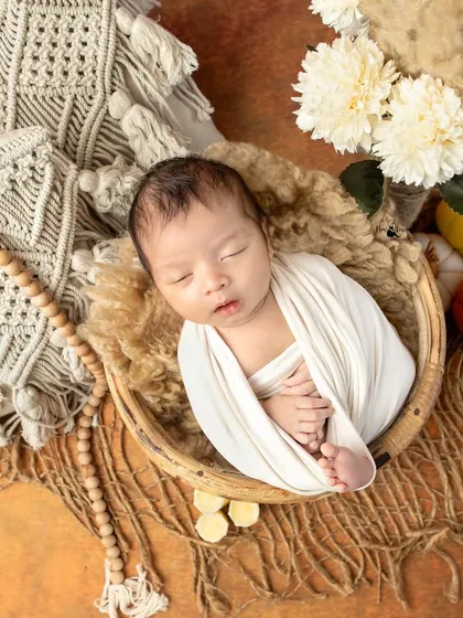 A classic newborn portrait using a simple white wrap and a rustic basket. This boho chic setup with macrame and natural textures creates a timeless and organic feel.