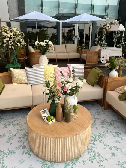 A serene and chic Haldi lounge setup with natural wood sofas, pastel-striped cushions, and fresh floral arrangements. A white cart adds a touch of whimsy.