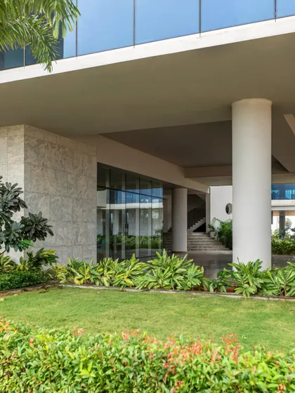 The ground-level entrance of the Pinnacle Campus, where the building's structure provides a shaded overhang above a lush lawn. This seamless transition between inside and outside is a core principle of our biophilic design philosophy.