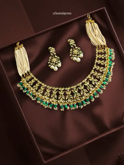 Luxury finds its true form in this intricately handcrafted Kundan choker. It blends rich textures of pearls, gleaming kundan work, and vibrant emerald drops, creating a statement of grace, tradition, and timeless beauty.